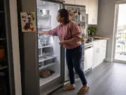 How to Organize a Refrigerator That Actually Lasts Woman reaching into an organized refrigerator with clear bins and labeled zones on every shelf