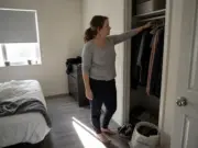 How to Organize a Small Bedroom in Five Steps Woman mid-way through organizing a small bedroom, donation bag on the floor and closet open