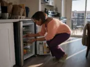 How to Organize a Small Fridge When Bins Don’t Fit Woman organizing a small apartment fridge with shallow shelves in a rental kitchen