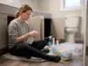 Cleaning Supplies Under the Sink? Store Them Safely Woman sorting cleaning supplies under a bathroom sink into clear stackable bins on the floor
