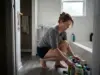Shower and Bath Organization That Survives Daily Use Woman sorting shower bottles on a tub ledge during a bathroom reset in a small rental apartment