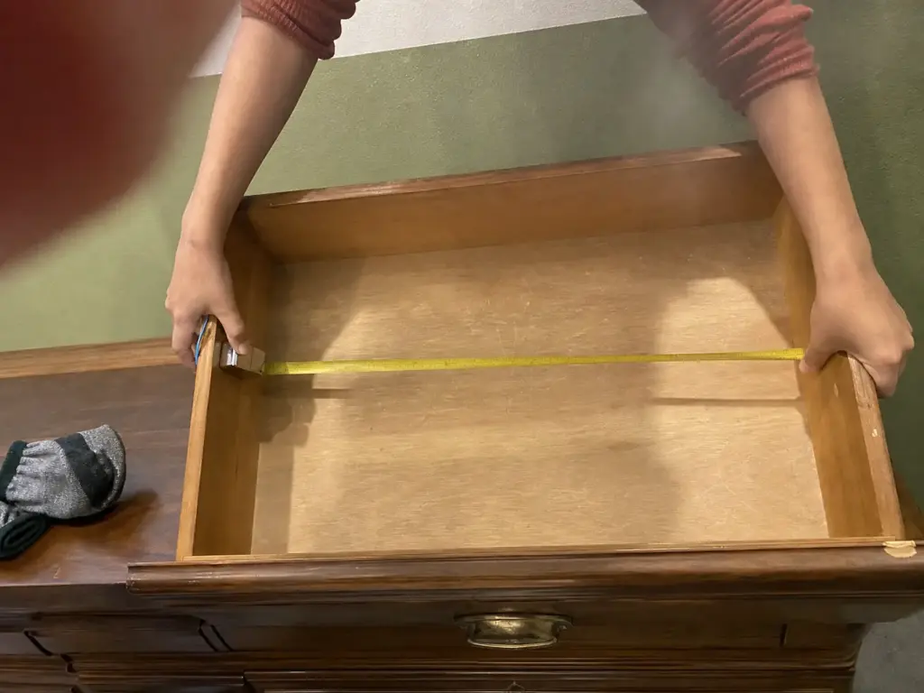 Best Drawer Dividers for Dressers That Actually Fit 1 Close-up of a tape measure housing pressed flat against the inside wall of an empty dresser drawer