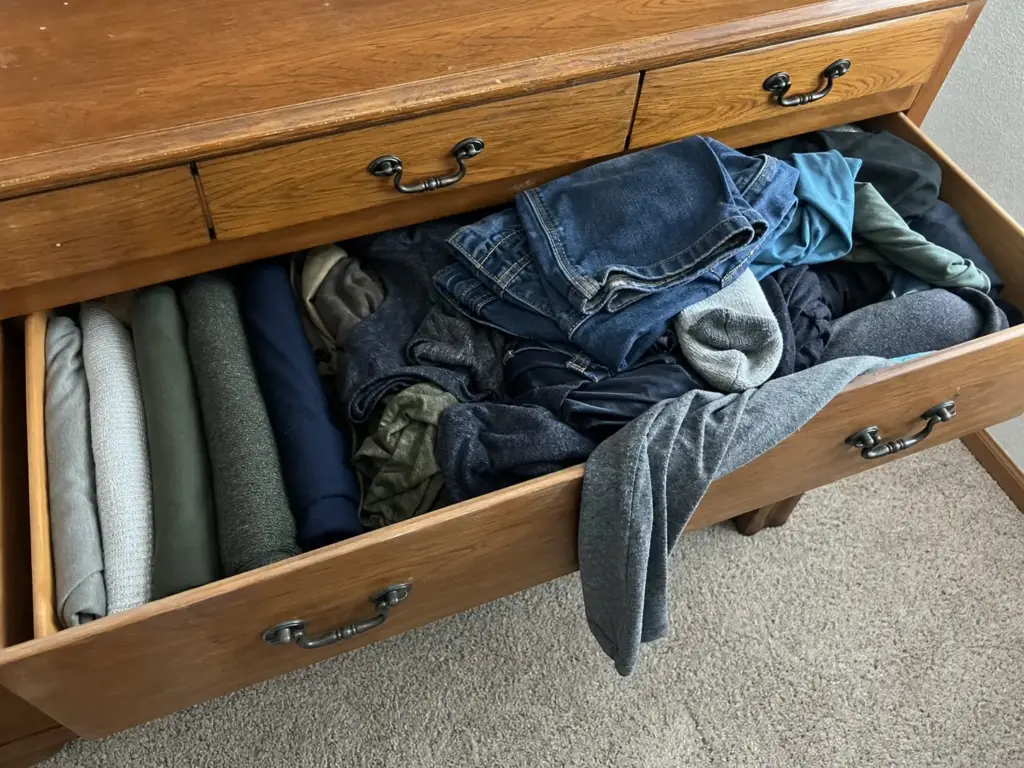 Open dresser drawer where neatly filed clothes have collapsed into a shoved pile