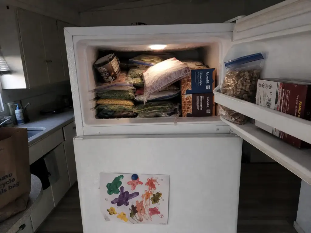 Overstuffed over-fridge freezer with stacked bags leaning off the shelf, the freezer avalanche problem