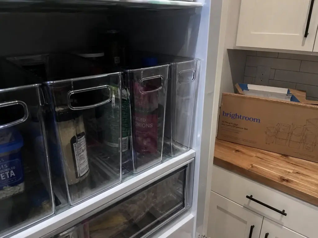 Overpacked refrigerator shelf where a tall bin nearly touches the glass shelf above it