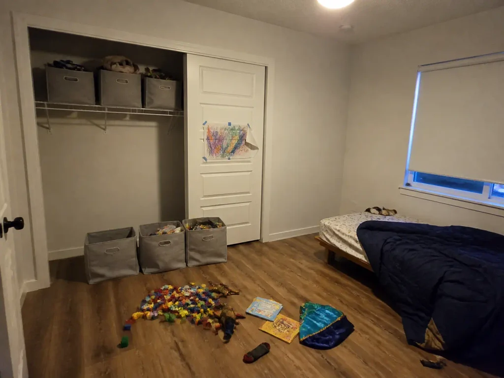Half-empty matching storage bins beside a new floor pile in a kids room three weeks later