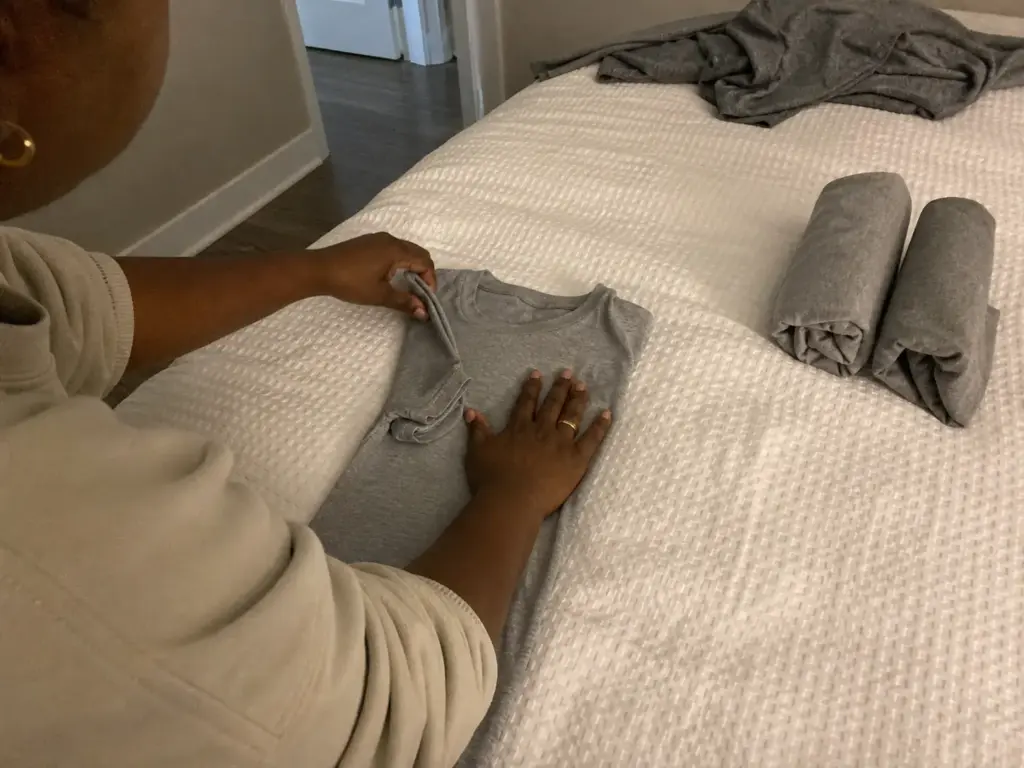 Hands folding a t-shirt into a standing KonMari fold on a bed, mid-sequence