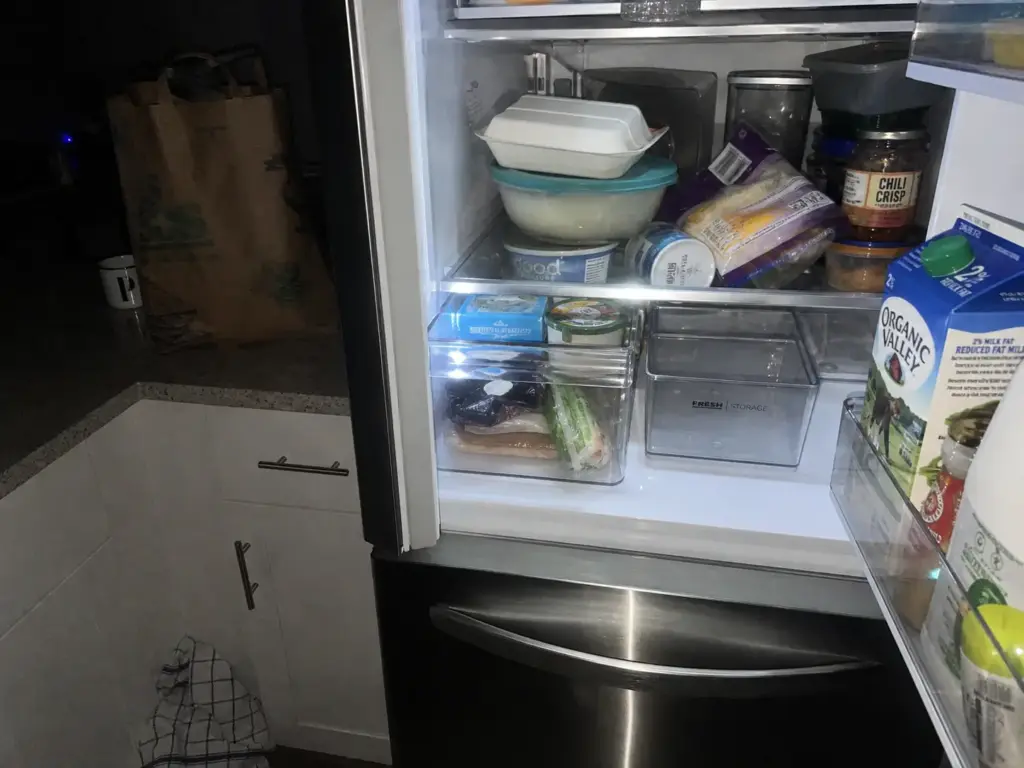 Fridge a month after organizing with bins shoved aside and containers stacked wherever they fit