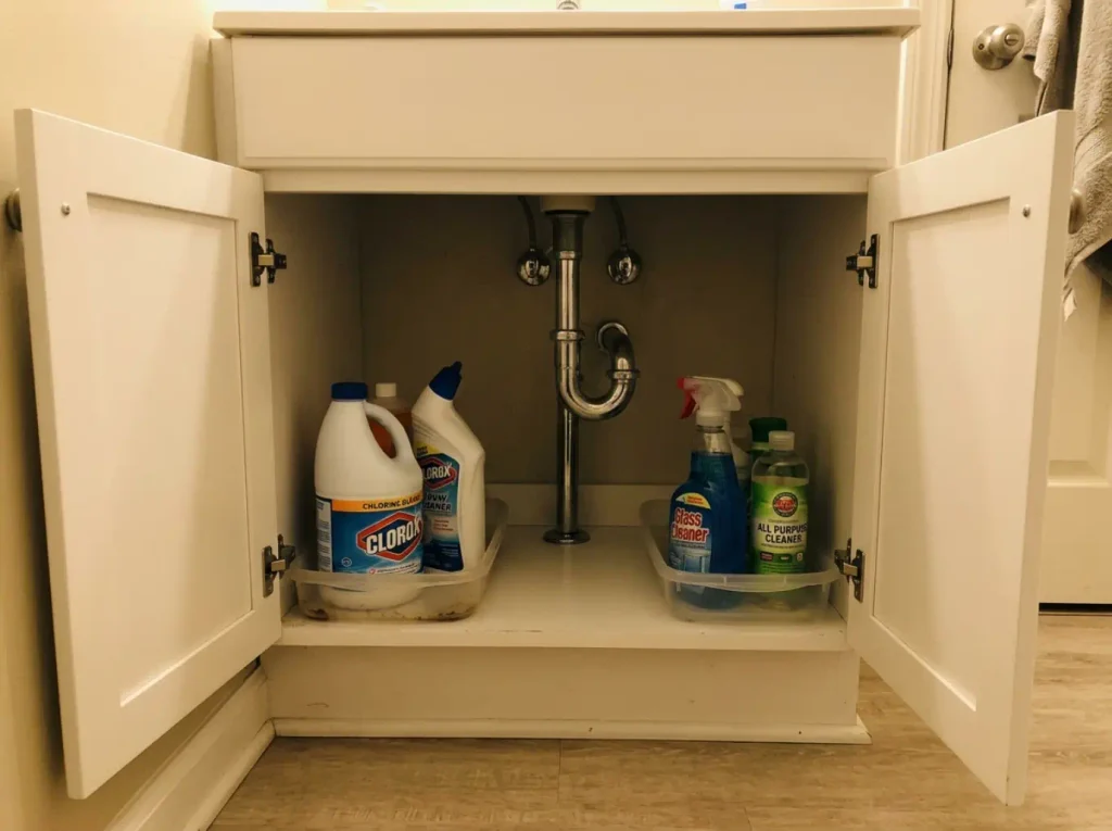 Cleaning Supplies Under the Sink? Store Them Safely 2 Bleach and glass cleaner bottles stored in separate contained zones on opposite sides of a cabinet