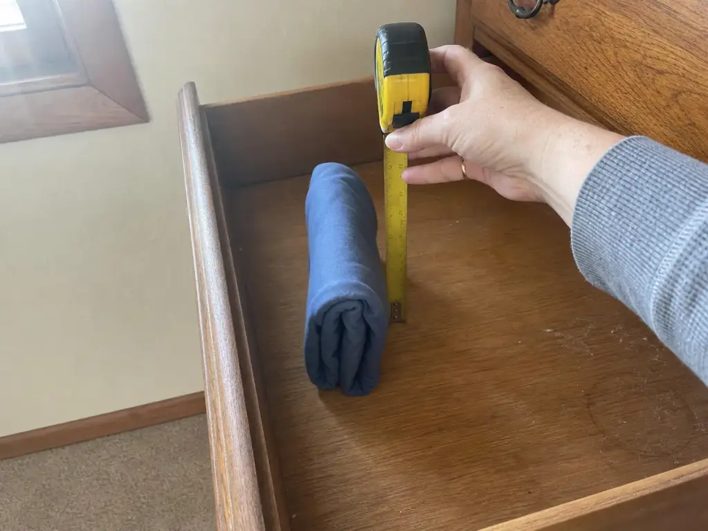 Tape measure held upright inside an open drawer beside a file-folded shirt for scale
