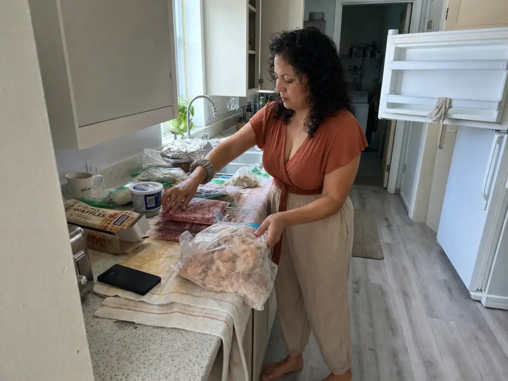 Woman sorting frozen food into keep and toss piles on a towel-covered counter during a freezer purge
