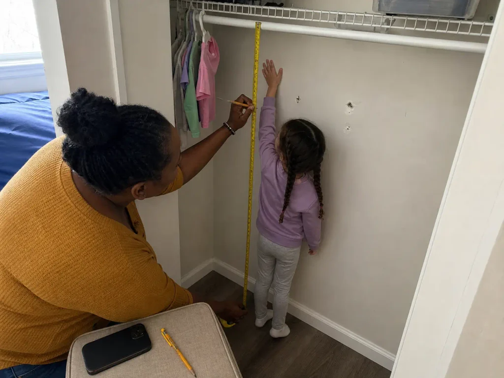 Measuring a child's reach height in a closet with a tape measure before organizing