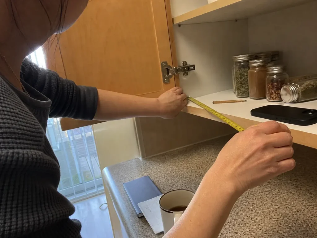 How to Organize Spices in a Small Kitchen Without a Rack 2 Hands measuring cabinet shelf depth with a tape measure before buying a spice organizer