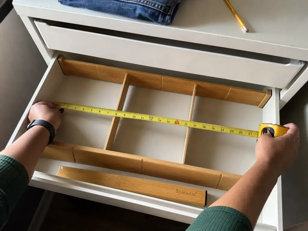 Hands measuring the inside depth of a dresser drawer with a tape measure before fitting dividers