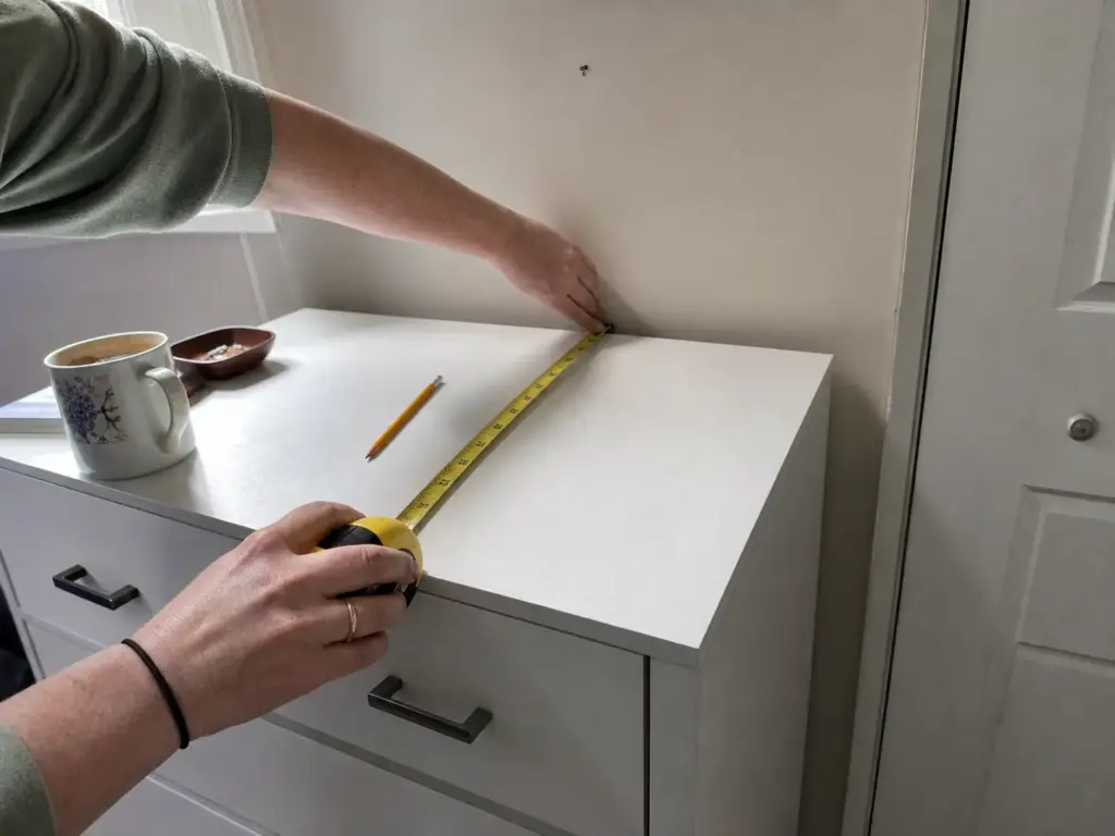 Hands measuring the depth of a dresser top with a yellow tape measure before buying organizers