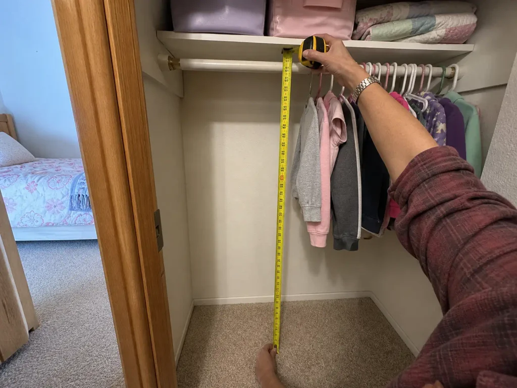 Hands measuring the closet rod height in a kids bedroom with a yellow tape measure