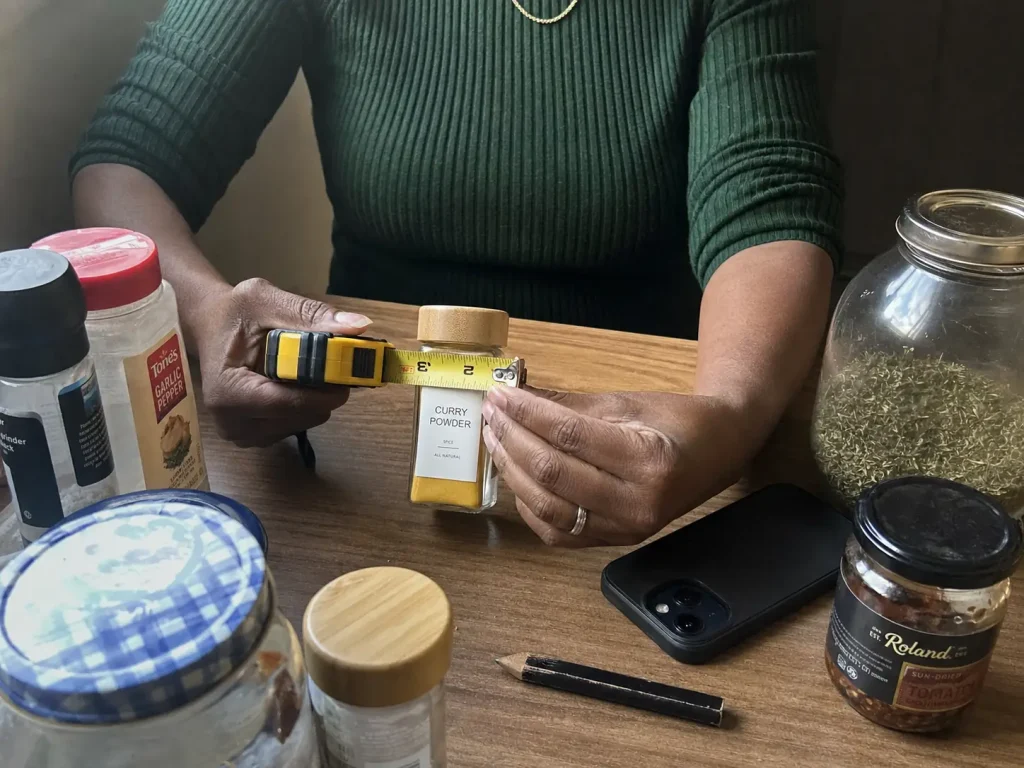 Hands measuring the diameter of a glass spice jar with a tape measure before building a DIY rack