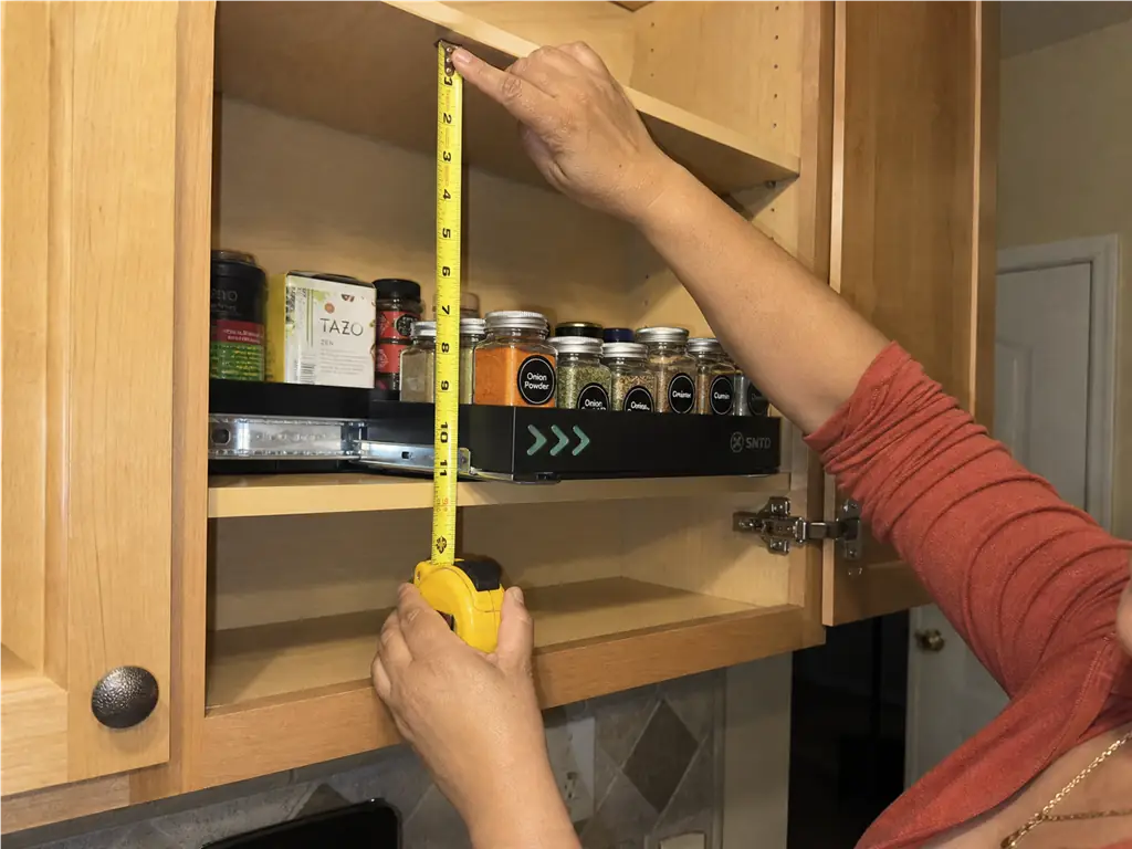 Spice Drawer vs Spice Rack? Your Tape Measure Decides 2 Hands measuring the vertical clearance inside an upper cabinet before installing a pull-out spice rack