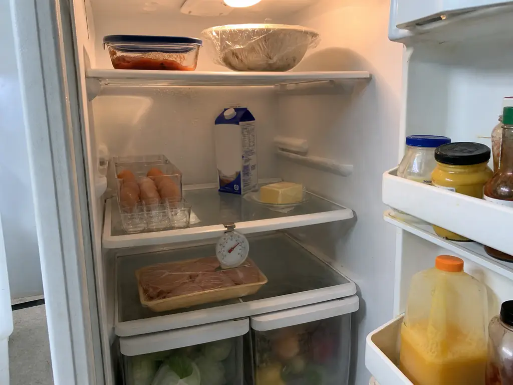 Open refrigerator with a free-standing appliance thermometer clipped to the middle shelf