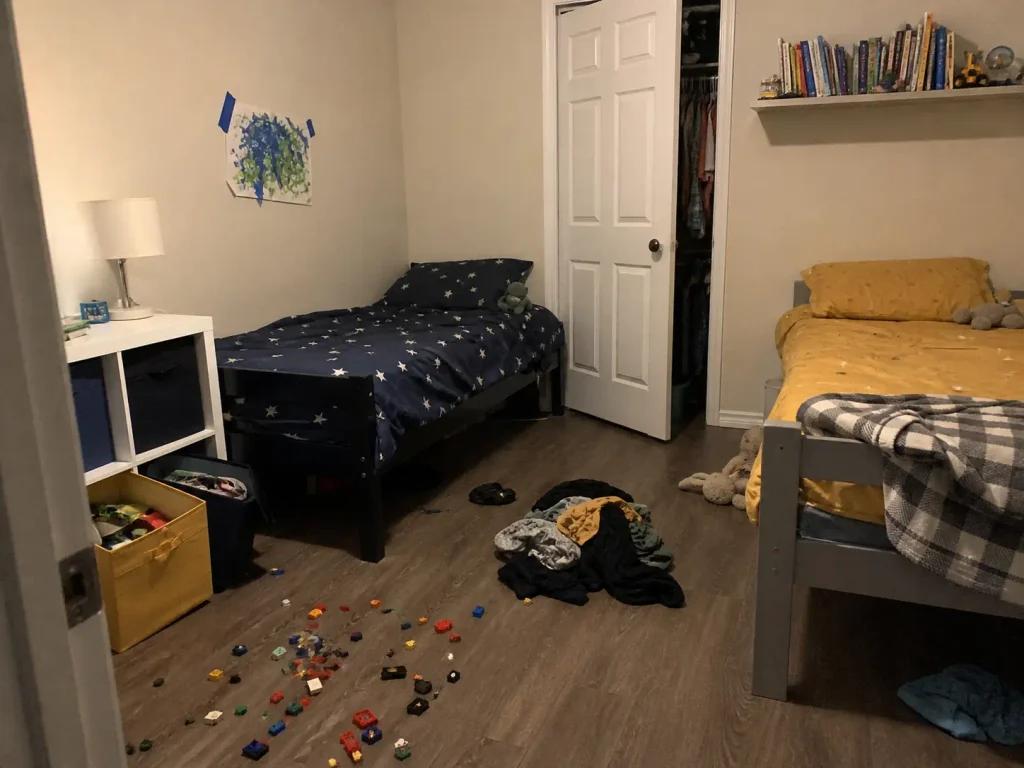Shared kids bedroom mid-revert with toys drifting across the floor boundary between two sibling zones