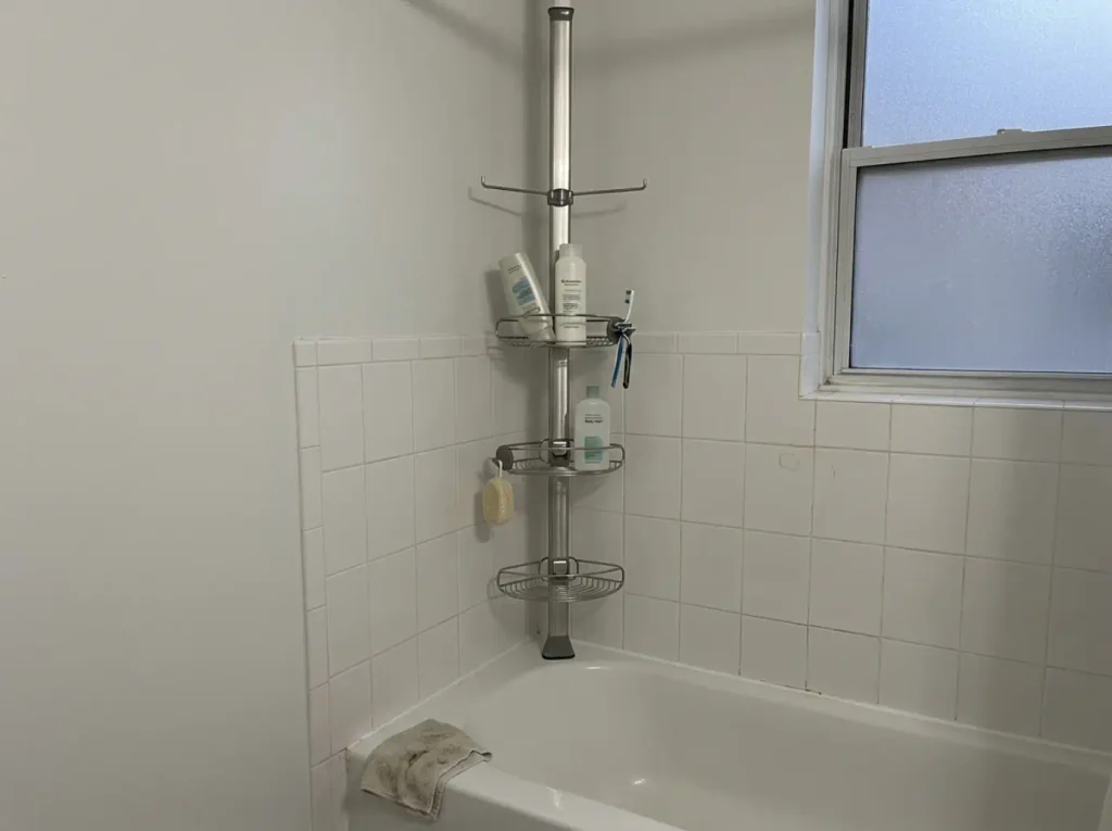 simplehuman tension pole shower caddy standing in the corner of a rental apartment tub