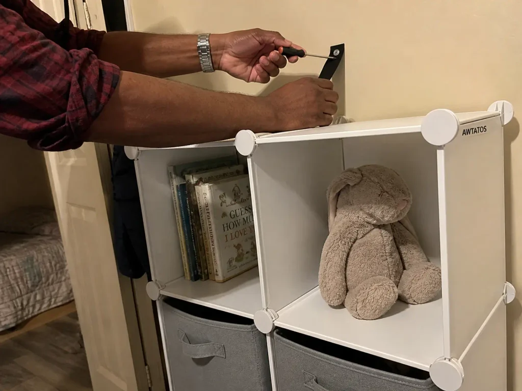 Hands anchoring a white cube storage organizer to a bedroom wall for vertical toy storage in a small space