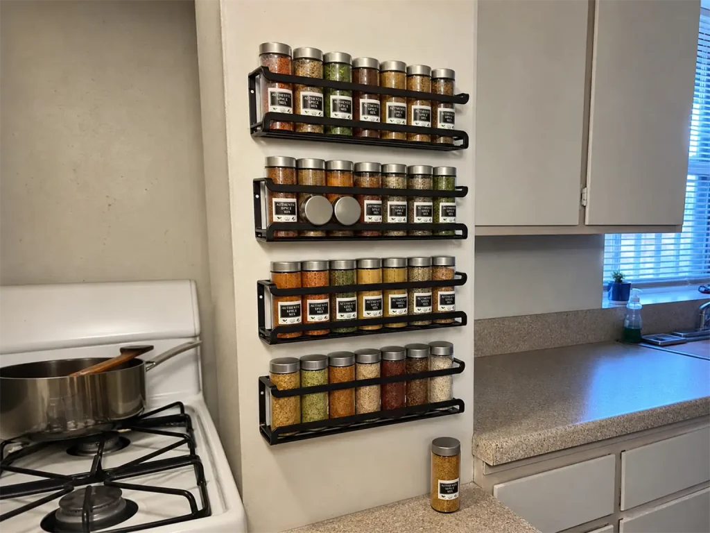 Best Spice Rack Organizers That Actually Stay Put 2 Wall-mounted spice rack strips holding jars on the narrow wall beside a rental stove