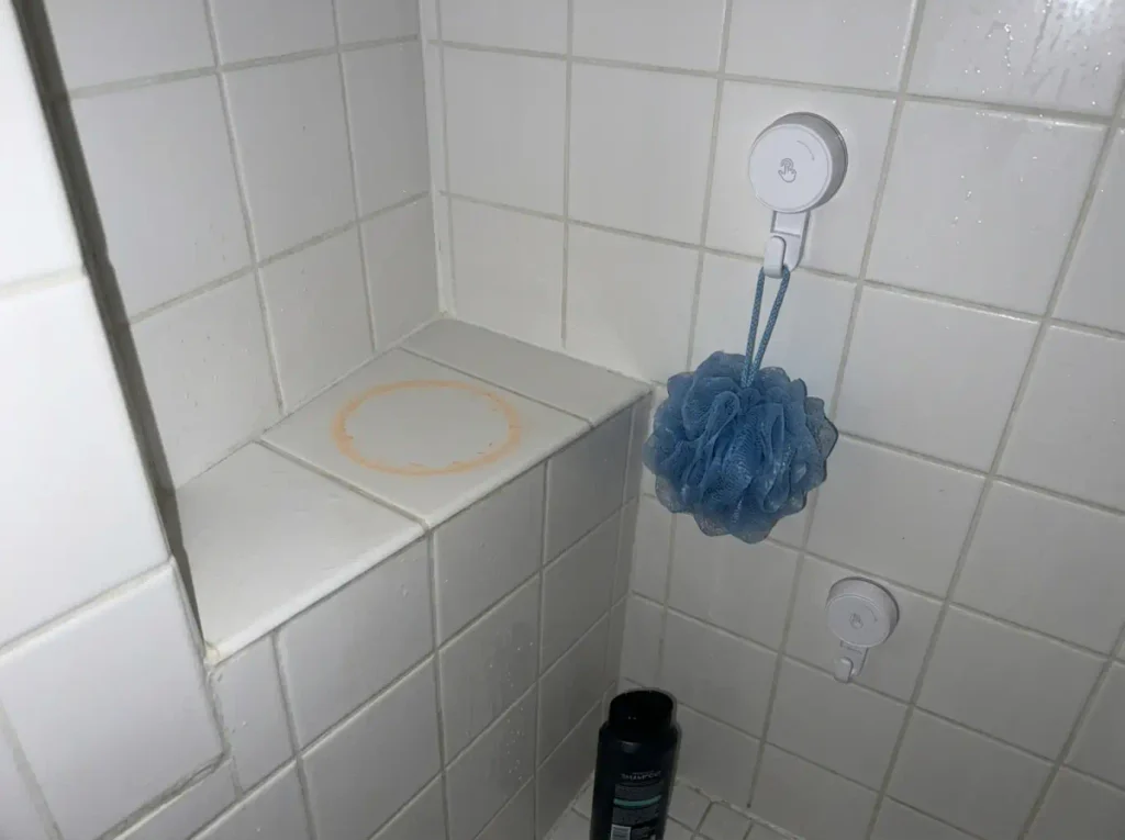 Suction shower hook and a mildew ring on a shower ledge showing why shower storage fails