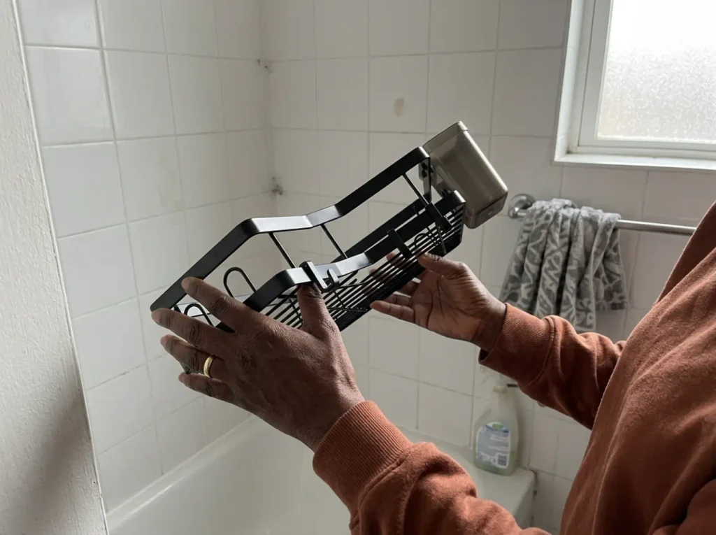 Hand holding an AKTECKE adhesive corner shower caddy before mounting it on smooth tile