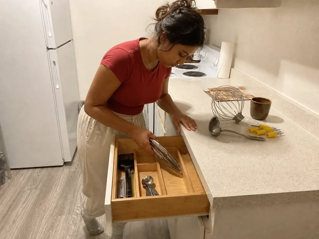 Why Your Small Kitchen With Few Drawers Stays Cluttered 3 Woman sorting kitchen tools into bamboo drawer dividers, deciding what stays in a small kitchen drawer