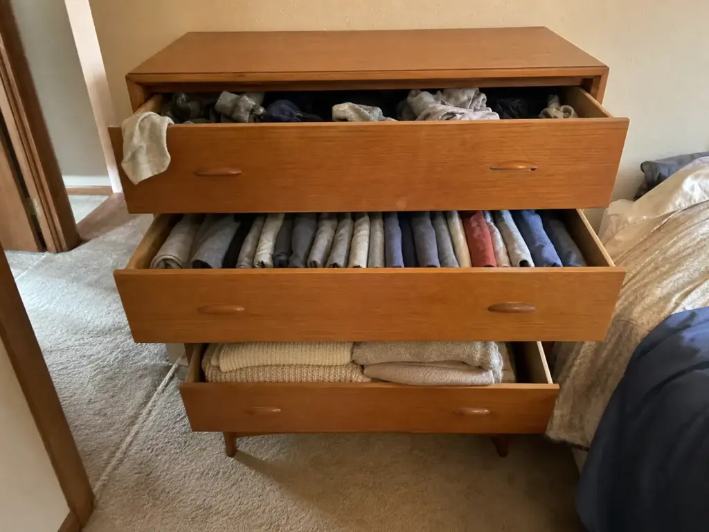 Dresser with three drawers open at different depths, each holding one category of clothing