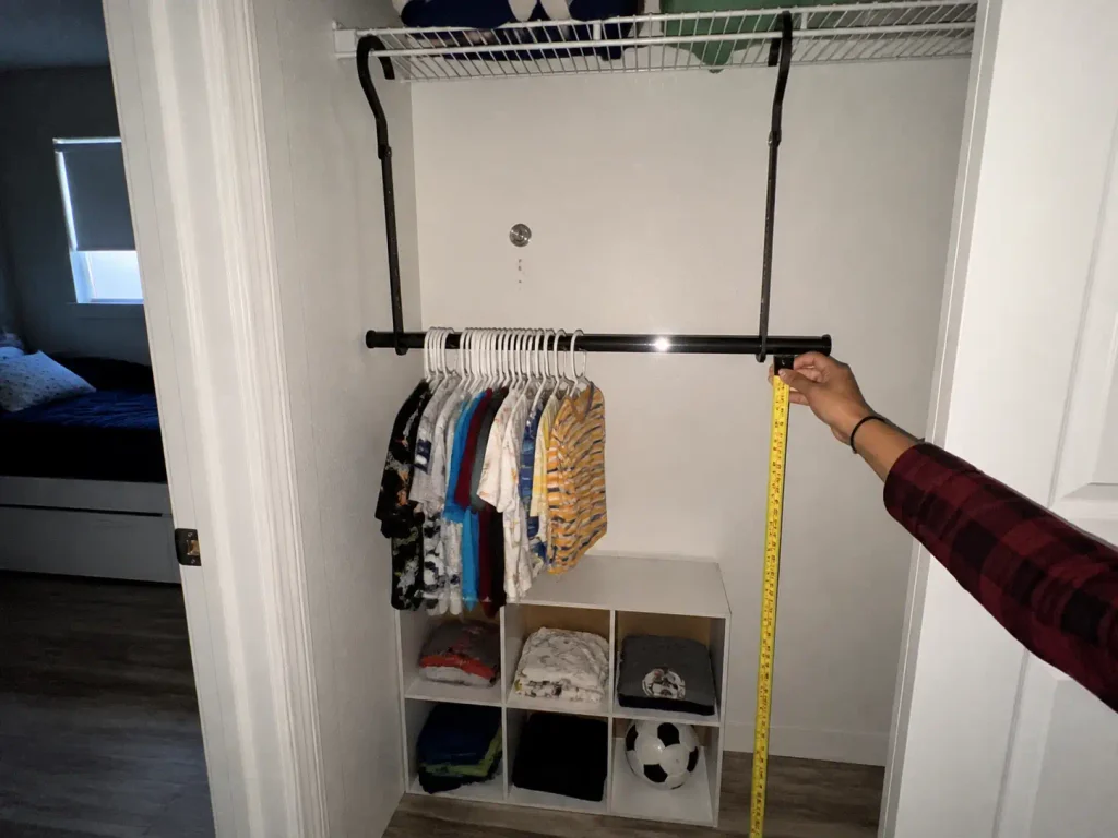 Second closet rod hung at child height with a tape measure checking the reach in a kids closet