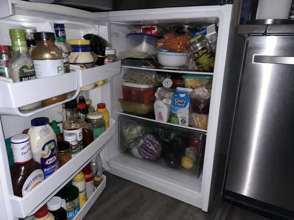Overpacked small fridge shelves blocking airflow with a thermometer at the back of a shelf