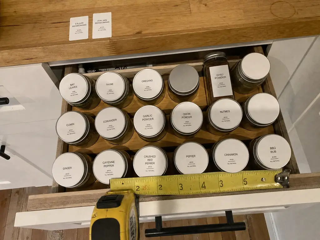 Open spice drawer viewed from above with round labels on jar lids and a tape measure