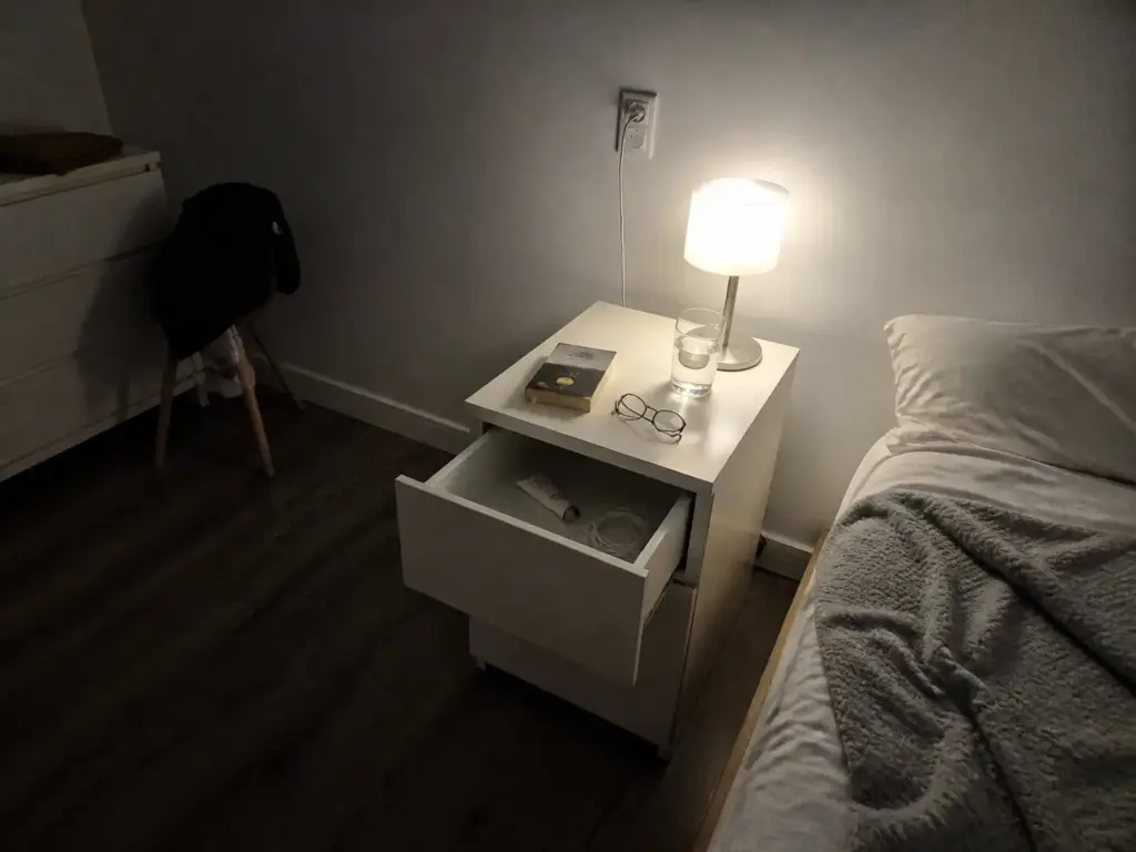 Small bedroom nightstand pared back to only arm's reach essentials beside the bed