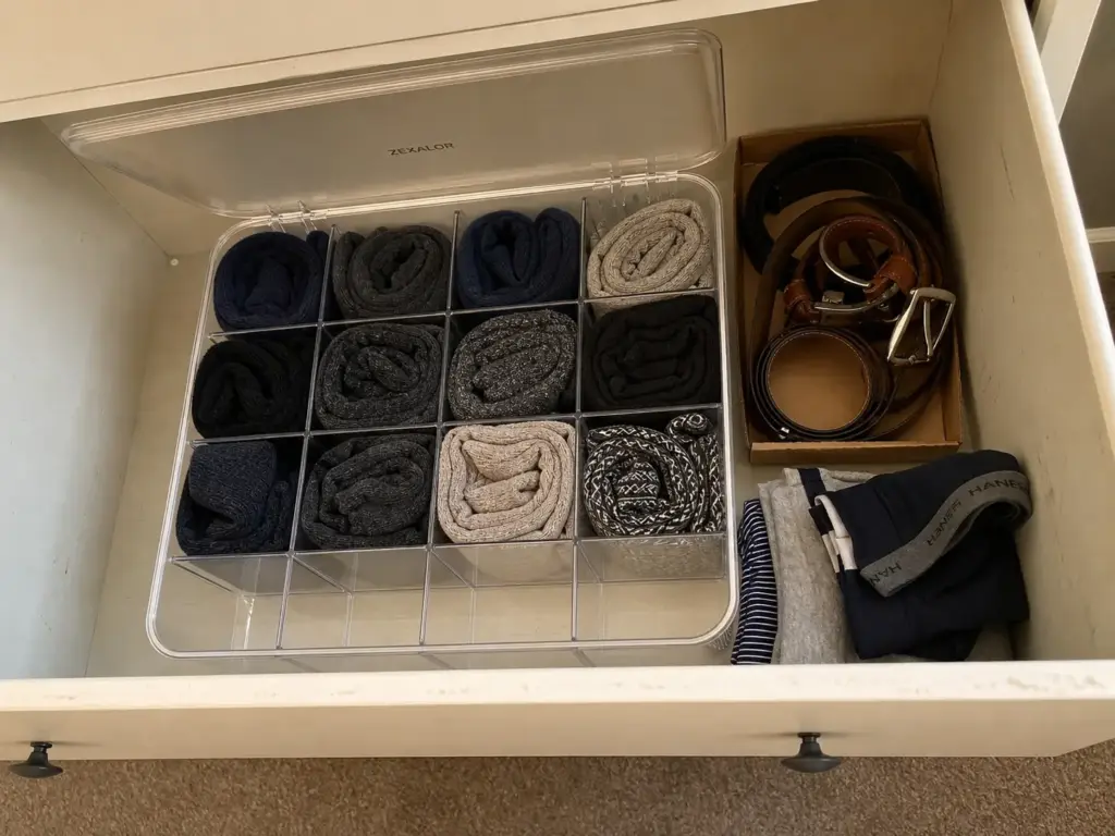 Compartment organizer bin holding rolled socks inside a shallow dresser drawer next to jewelry trays