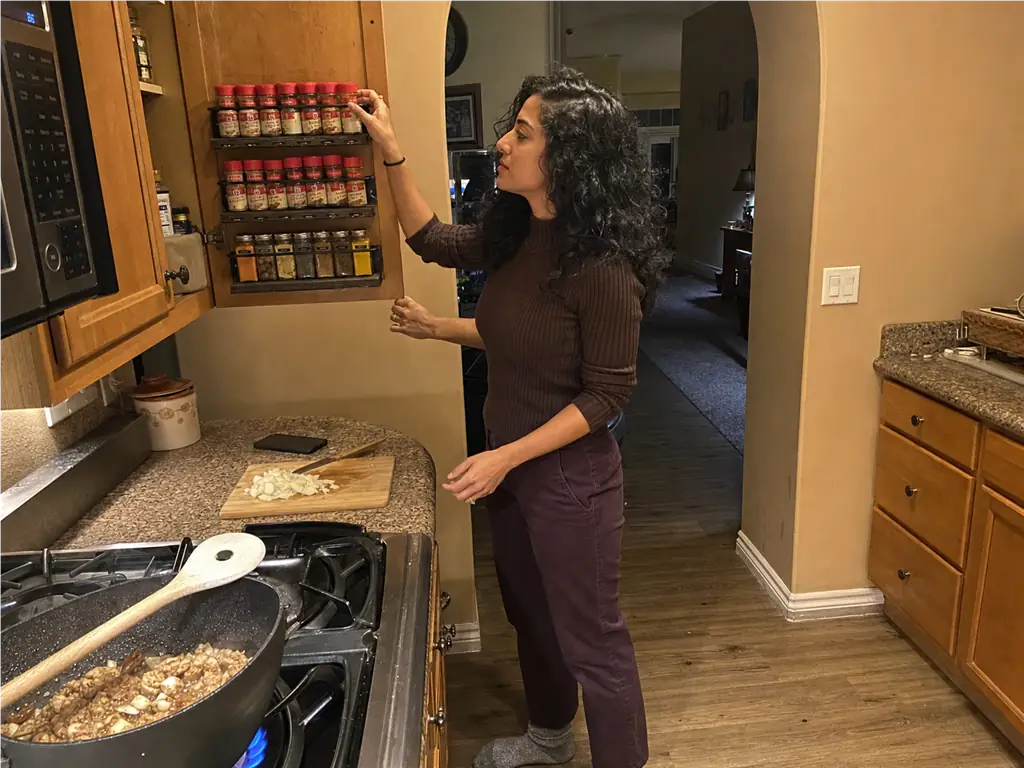 Spice Drawer vs Spice Rack? Your Tape Measure Decides 4 Woman grabbing a spice jar from a cabinet door rack mid-recipe while a pan cooks on the stove