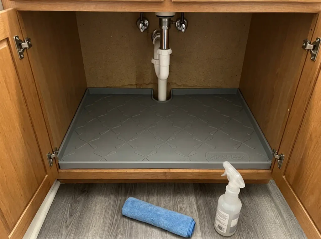 Waterproof under sink mat laid across a bathroom cabinet floor beneath the drain pipe