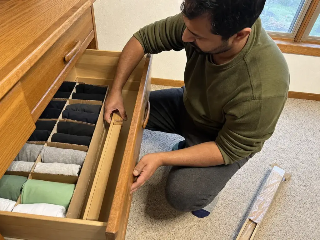 Man fitting an adjustable divider into a dresser drawer beside a cardboard divider grid