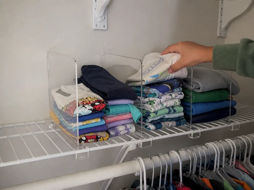 Acrylic shelf dividers keeping stacks of kids folded clothes separated on a closet shelf