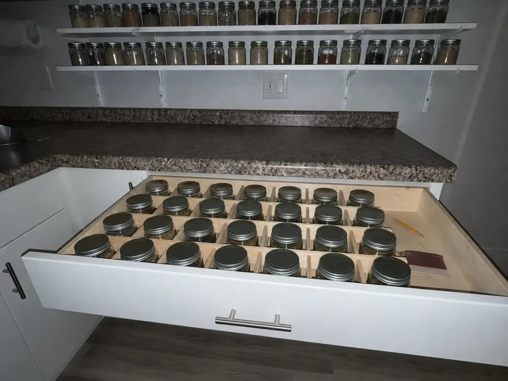 Open kitchen drawer with small spice jars set in a wood-strip grid, shot with direct flash