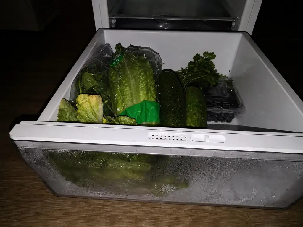 Crisper drawer pulled open showing the humidity slider vent and produce filling about two-thirds of the drawer