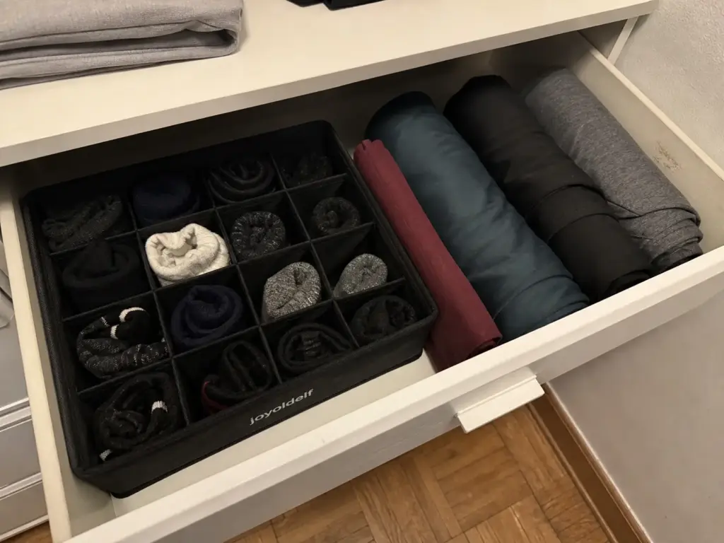 Sock drawer organizer tray with bundled socks beside rolled activewear in a dresser drawer