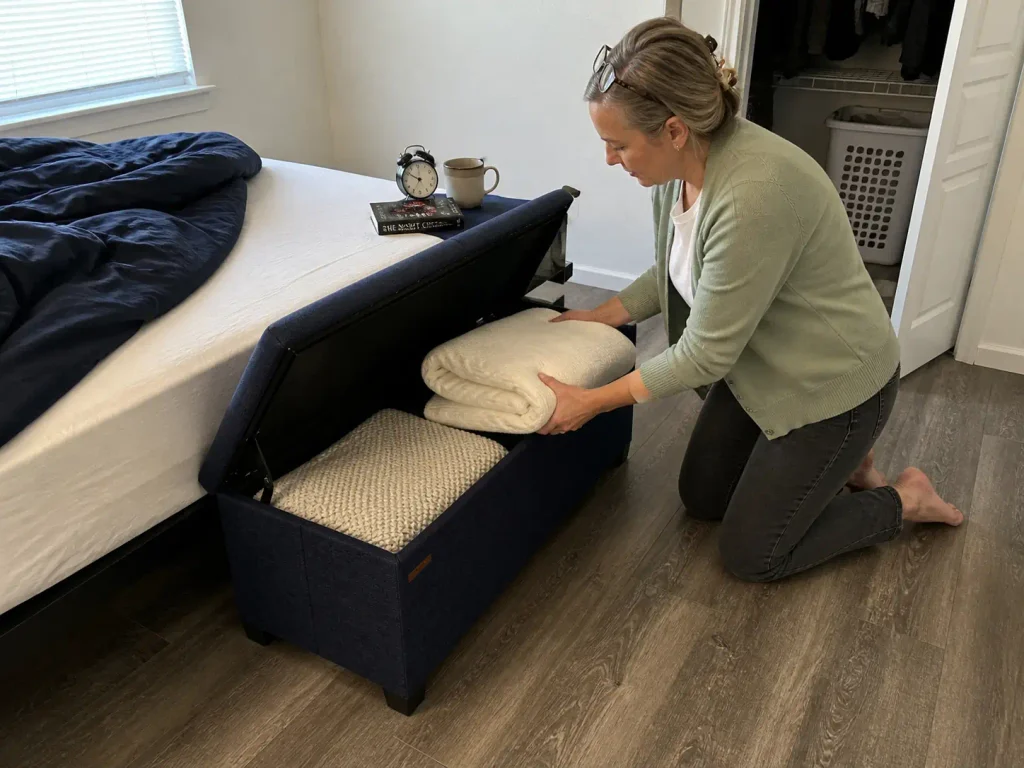 Storage ottoman used beside a bed as a nightstand alternative with blankets stored inside