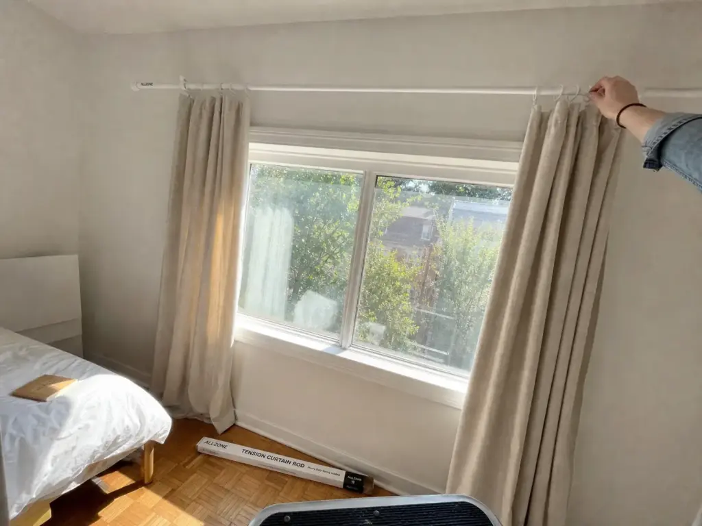 How to Make a Small Bedroom Look Bigger for Renters 4 Tension curtain rod mounted high above a small bedroom window with floor-length light curtains