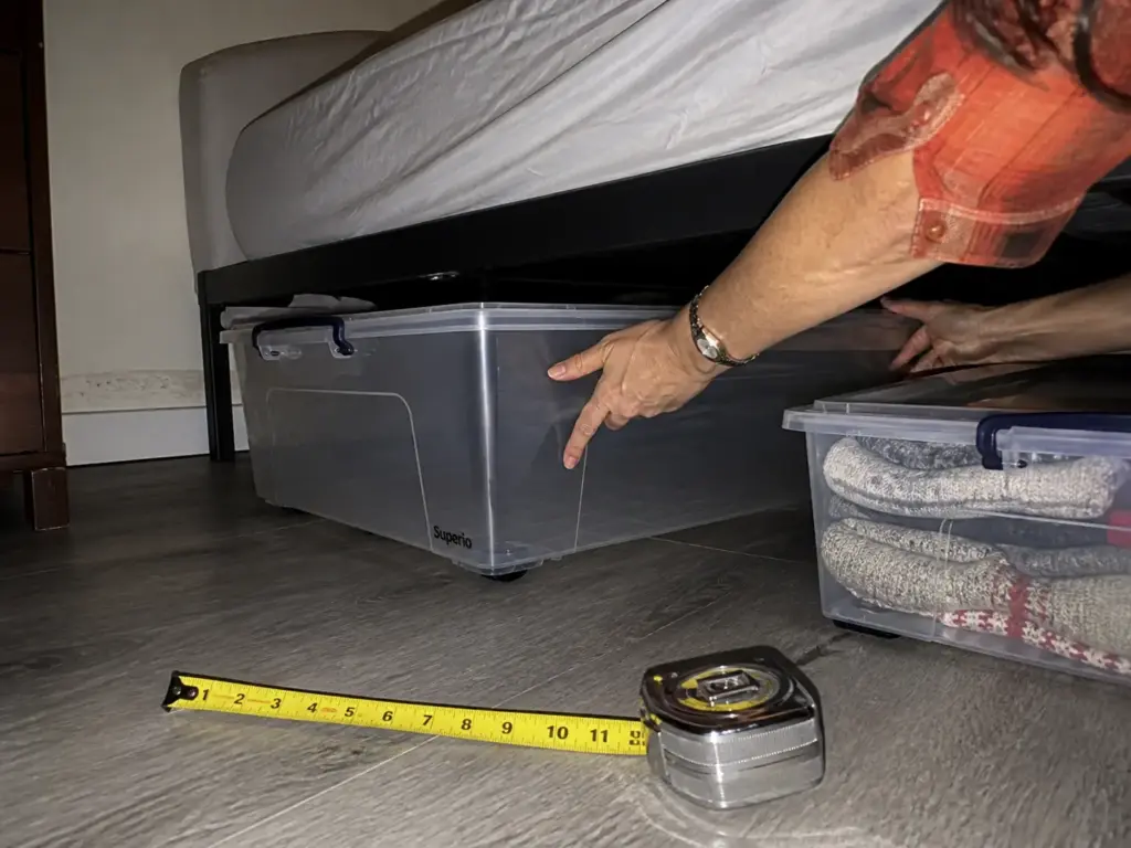 Hands sliding a rolling under bed storage container into the clearance under a bed frame