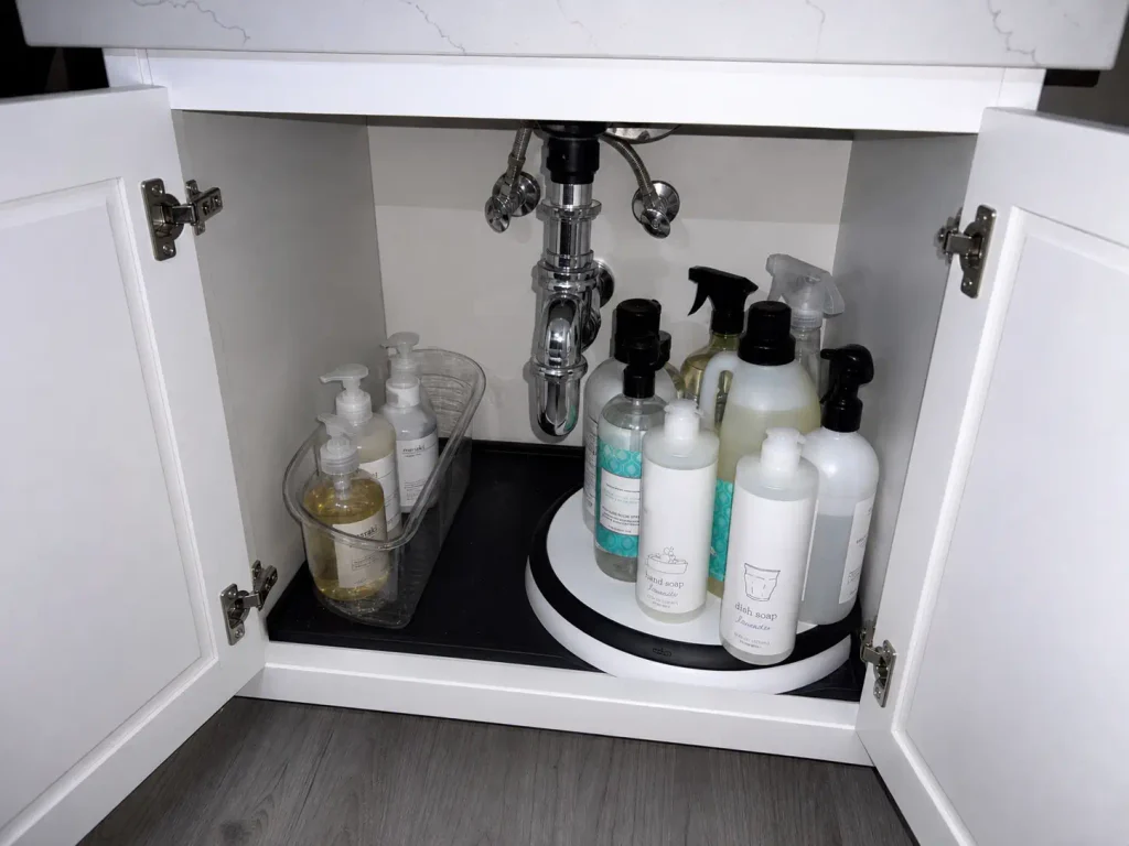 Open bathroom vanity cabinet with a lazy susan turntable and wedge bin fitted around the P-trap pipe