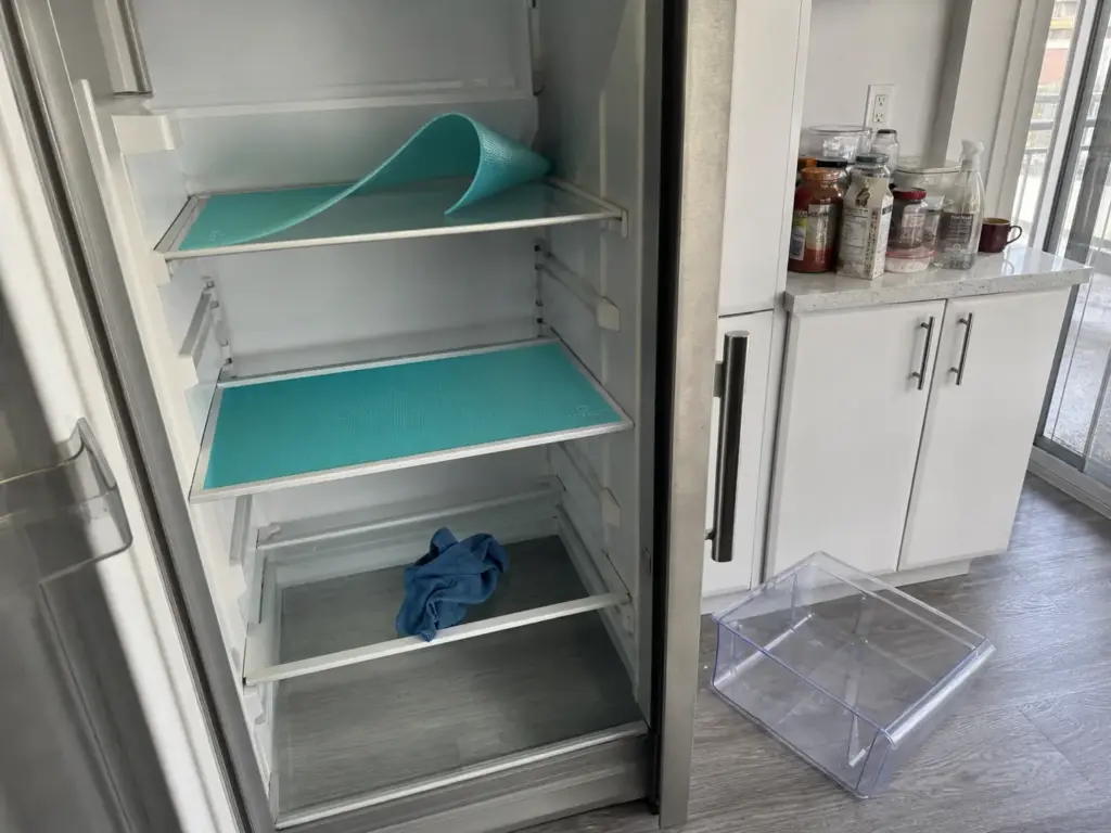 Empty refrigerator shelves being lined with washable mats during a full fridge clean-out