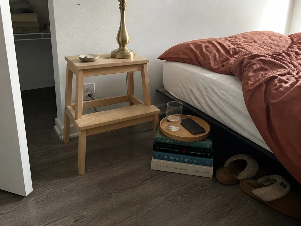 Wooden step stool and a stack of books with a tray used as free nightstand alternatives