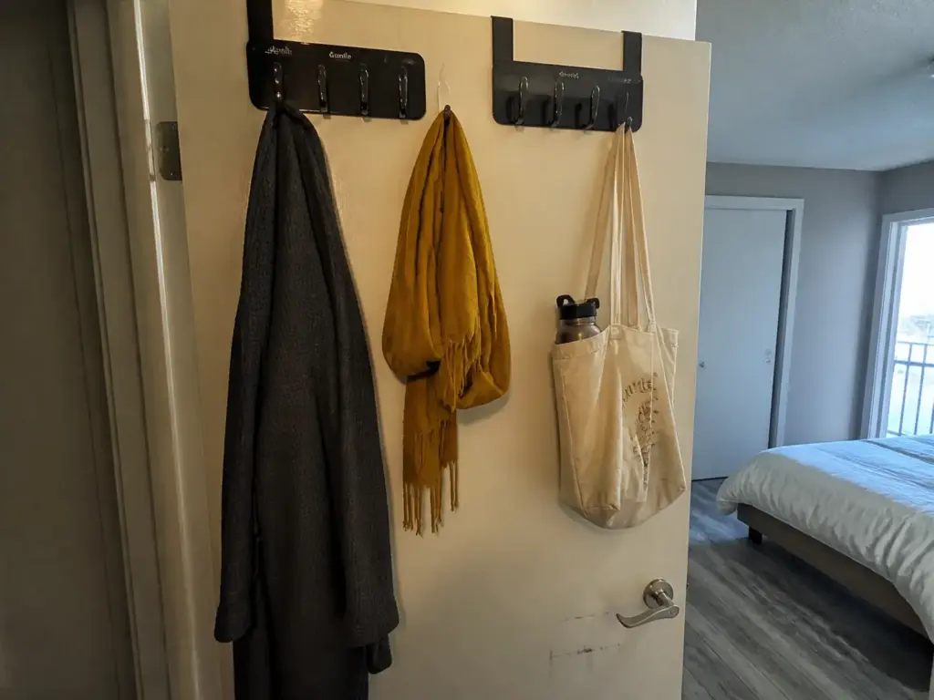 Felt-lined over-door hooks spread across a bedroom door holding a robe, tote bag and scarf